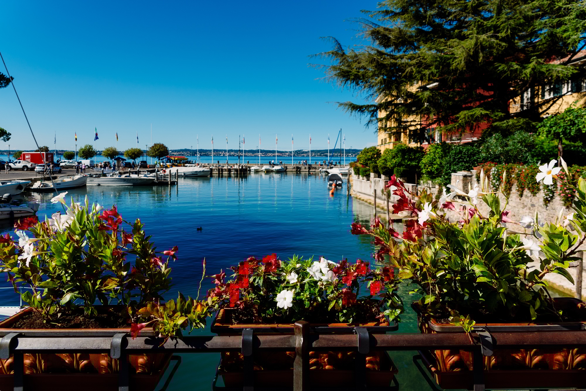 Boats moored next to Sirmione Castle on Lake Garda admired by tourists in summer.